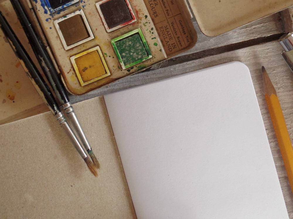 blank inside page of notebook with watercolor paint tray and brushes
