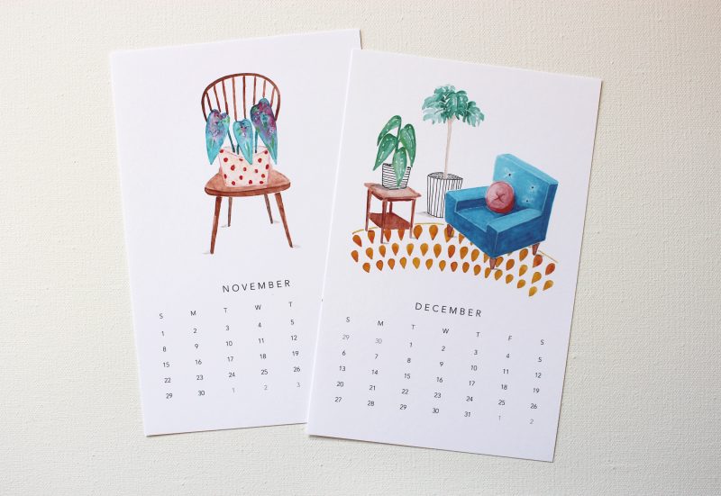 November and December of a plant lovers calendar with watercolors of a plant sitting on a chair in a polka dotted pot and a blue chair surrounded by plants on a orange and white patterned rug by messy bed studio