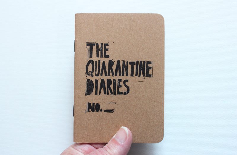 kraft colored quarantine journal with black ink in hand by messy bed studio