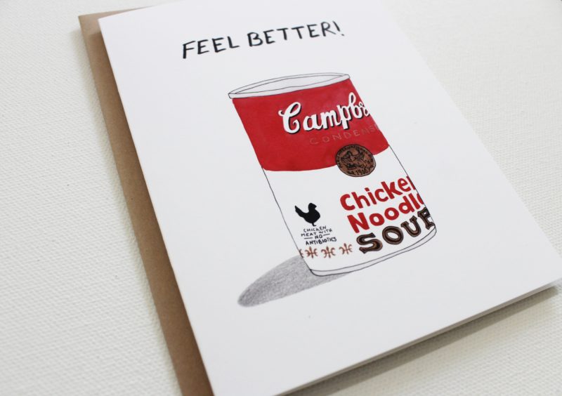 angled closeup of funny get well card with watercolor painted can of campbell's chicken noodle soup can with the words feel better