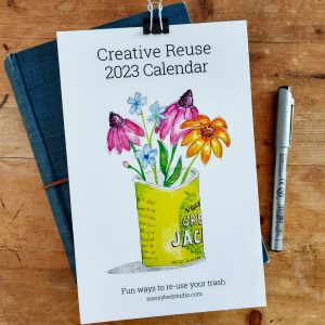 Cover of Creative Reuse 2023 Calendar resting on a book with a pen next to it