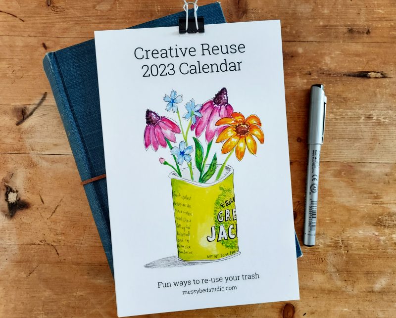 Cover of Creative Reuse 2023 Calendar resting on a book with a pen next to it